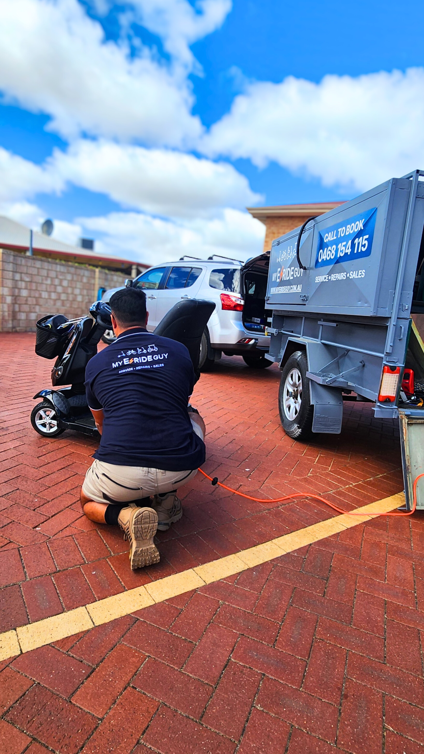 Mobile scooter repair service by My ERide Guy, technician servicing a mobility scooter outdoors, parked vehicle and trailer in background, emphasizing convenience and accessibility.