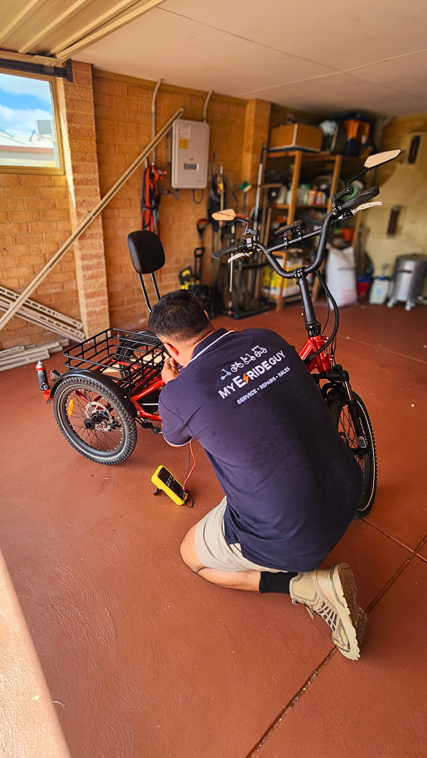 Technician from My E-Ride Guy performing maintenance on a red e-bike in a garage, using diagnostic tools for repairs and adjustments.